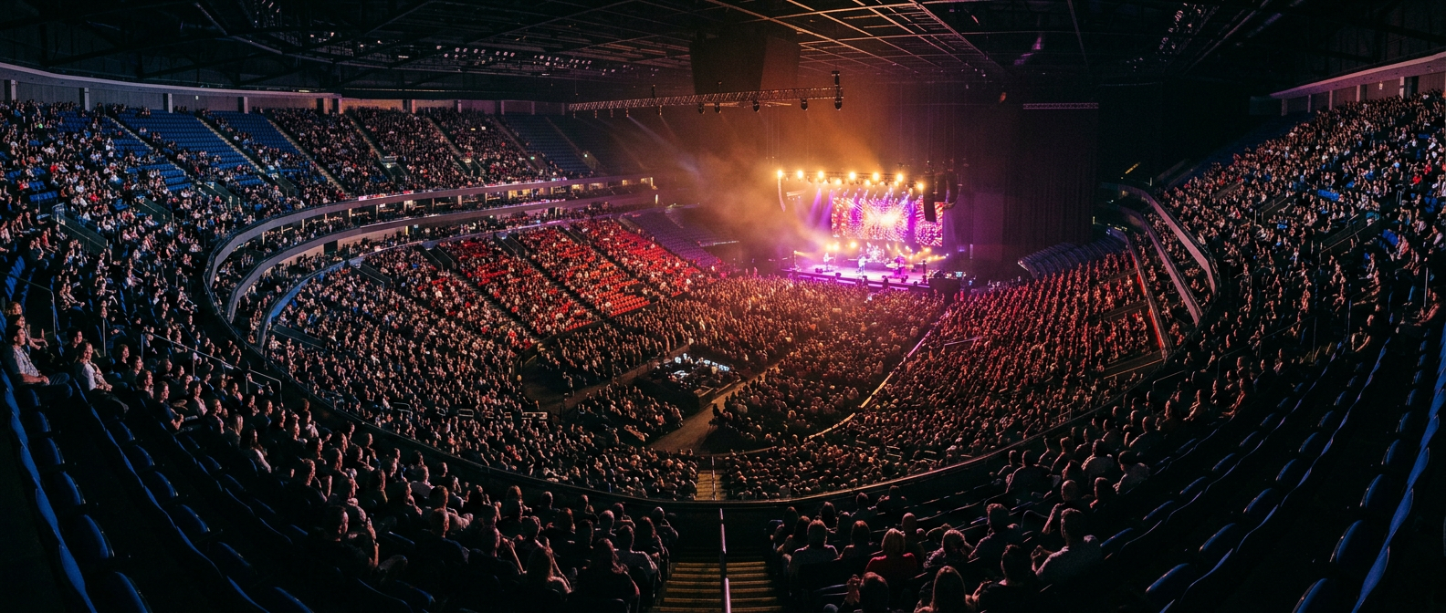 A large concert arena seen from the upper tiers, the stage lit in orange and magenta